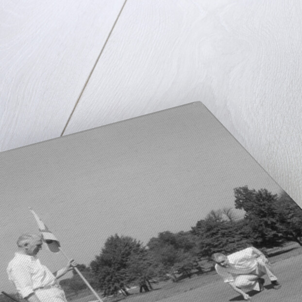 1930s 1940s elderly men on golf green one holding flag the other kneels lining up his putt by Anonymous