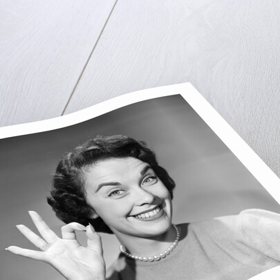 1950s woman smiling wearing pearl necklace looking at camera making okay gesture with hand by Anonymous