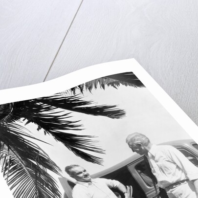 1930s 2 elderly men standing by car carrying golf bag palm tree frond in corner by Anonymous