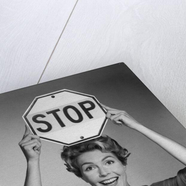 1950s 1960s smiling woman holding stop sign above her head looking at camera by Anonymous