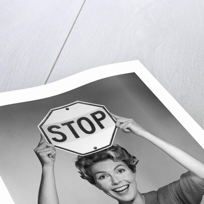 1950s 1960s smiling woman holding stop sign above her head looking at camera by Anonymous