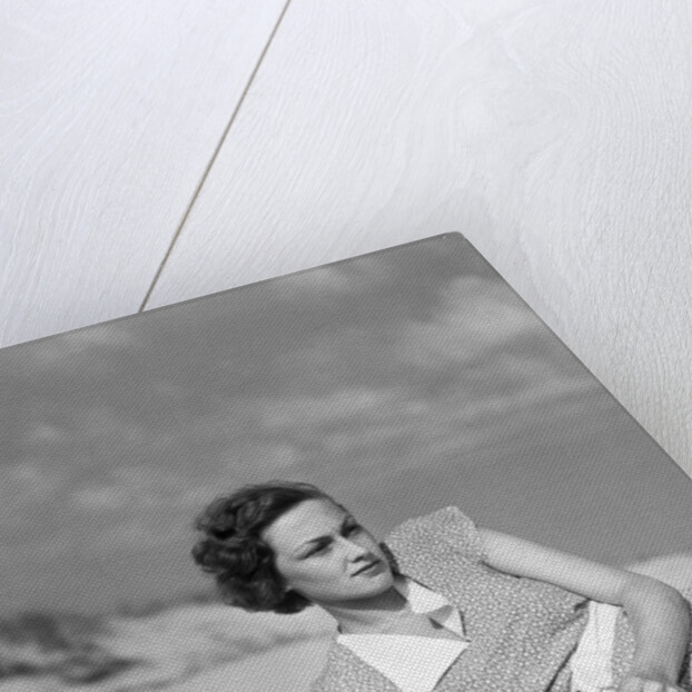1930s woman leaning in wooden chair on beach wearing printed dress holding magazine looking thoughtful by Anonymous