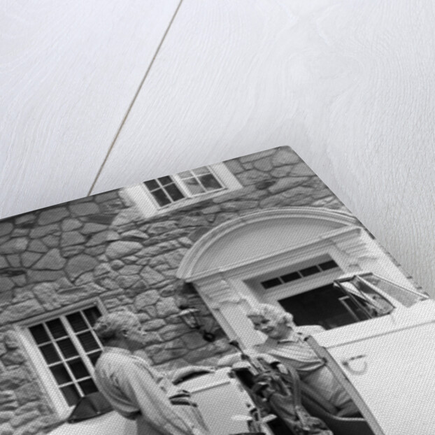 1940s senior retired couple loading golf clubs into white convertible car in front stone house by Anonymous