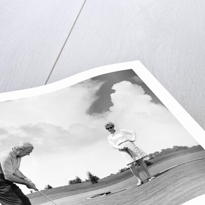 1960s older couple on golfing green man putting by Anonymous