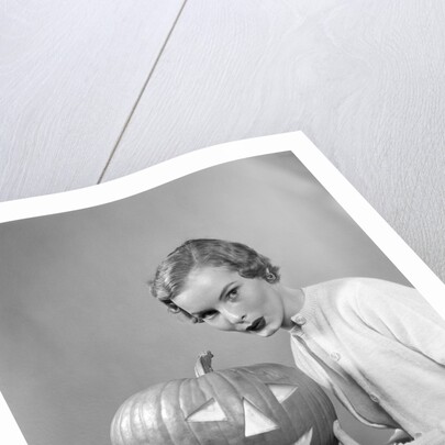 1950s woman wearing sweater holding carved pumpkin jack-o-lantern on her lap by Anonymous