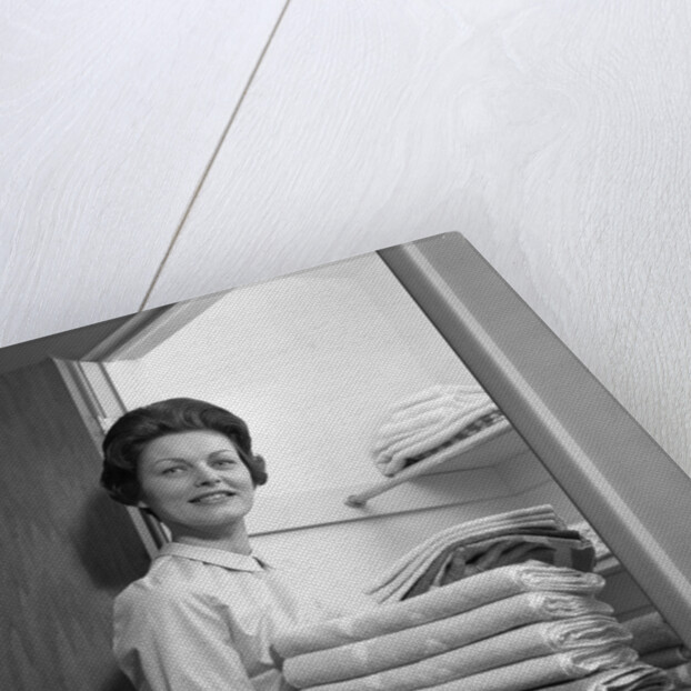 1950s 1960s housewife holding laundry folded towels by linen closet looking at camera by Anonymous