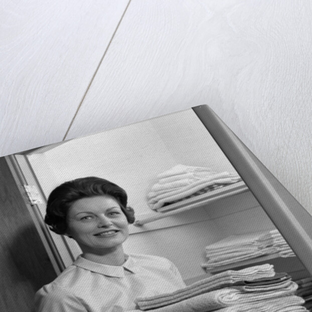 1960s woman holding laundry folded towels by linen closet looking at camera by Anonymous