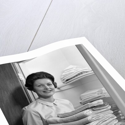 1960s woman holding laundry folded towels by linen closet looking at camera by Anonymous