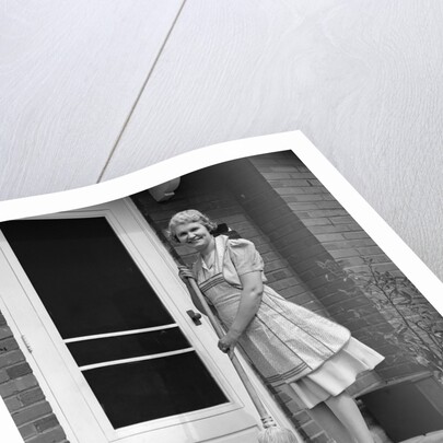 1940s smiling woman sweeping porch front door step with a broom looking at camera by Anonymous