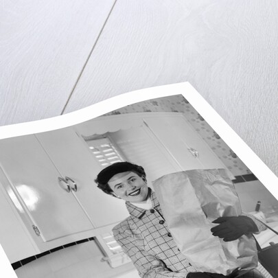 1950s smiling woman in kitchen holding grocery bag handbag wearing hat gloves looking at camera by Anonymous