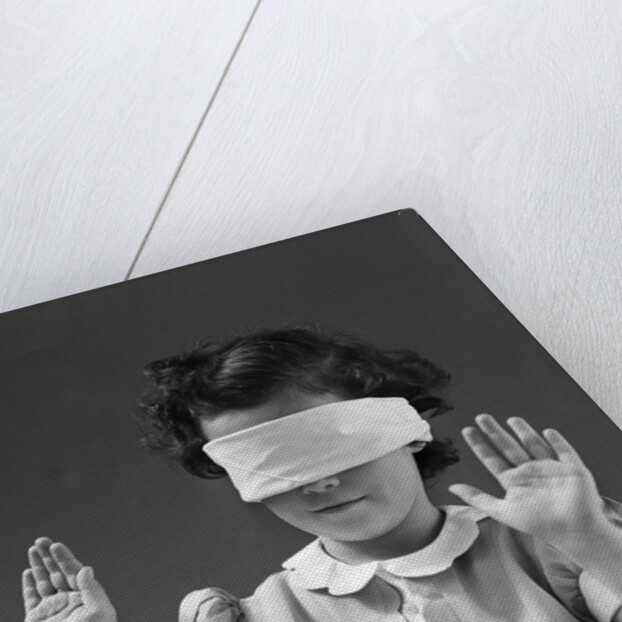 1940s child wearing blind fold with hands up in the air by Anonymous
