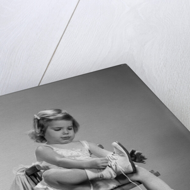 1960s little girl putting on shoes sitting on chair by Anonymous
