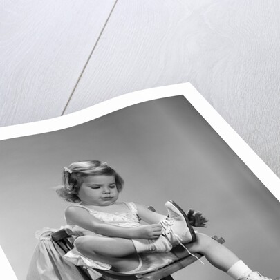 1960s little girl putting on shoes sitting on chair by Anonymous