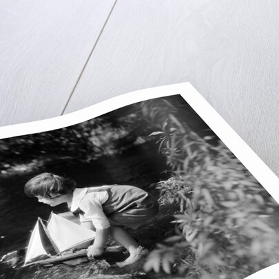 1920s boy putting toy sailboat into stream by Anonymous