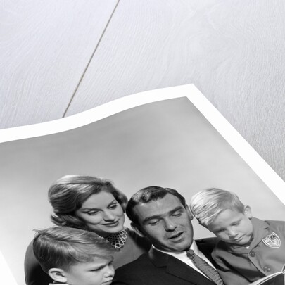 1960s family father mother sons reading book together by Anonymous
