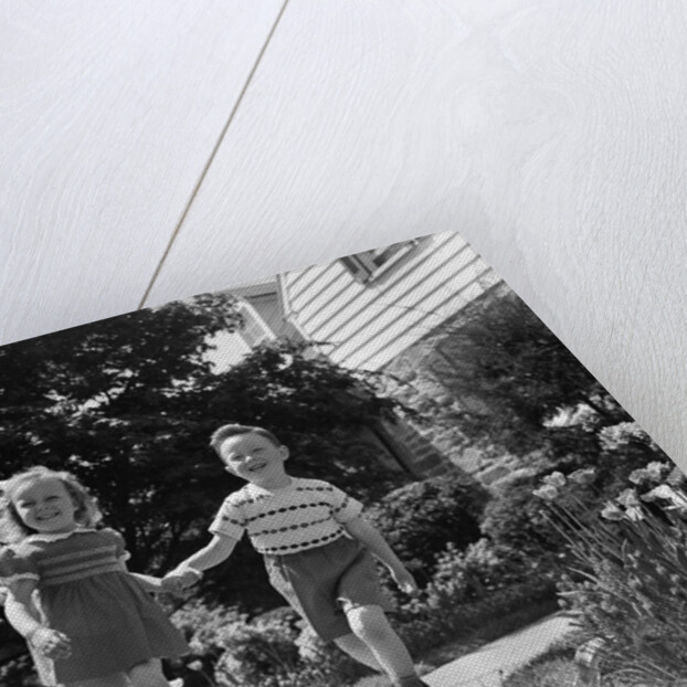 1950s two children holding hands smiling walking along sidewalk by Anonymous