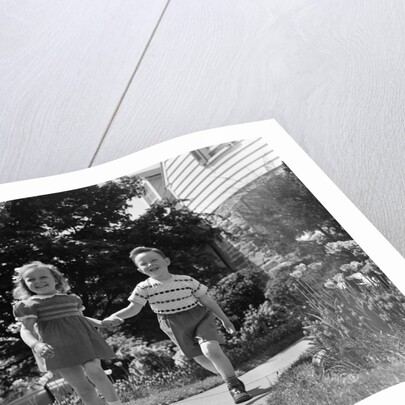 1950s two children holding hands smiling walking along sidewalk by Anonymous