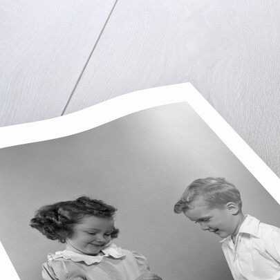 1950s little girl and boy putting coin into piggy bank by Anonymous