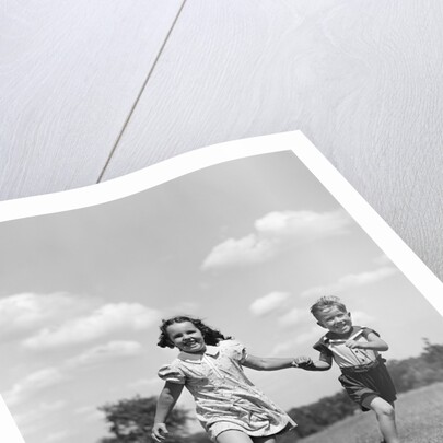 1940s two smiling children running holding hands in grassy field by Anonymous