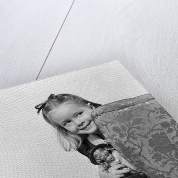 1940s little girl holding doll peeking around side of chair by Anonymous