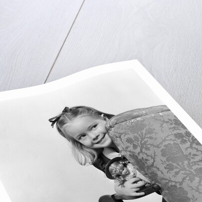 1940s little girl holding doll peeking around side of chair by Anonymous