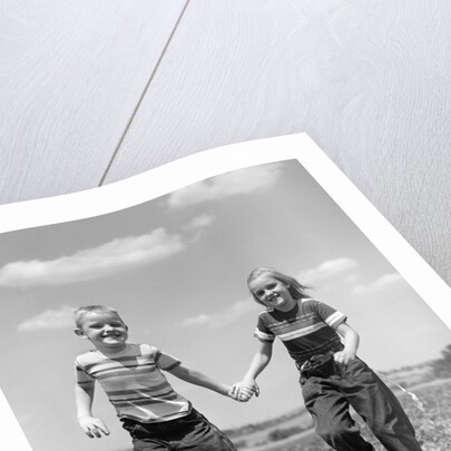 1950s boy girl running grassy farm field holding hands by Anonymous