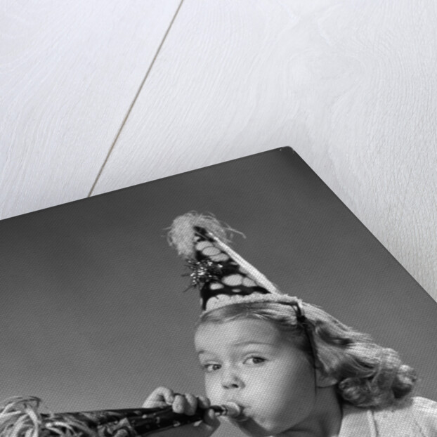 1950s girl wearing party hat blowing into noise maker looking at camera by Anonymous