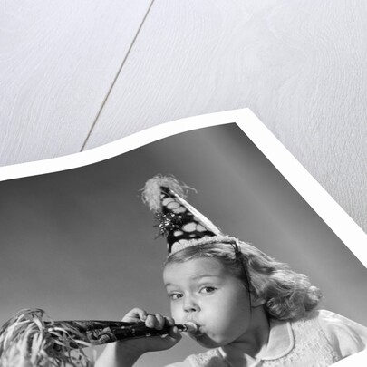 1950s girl wearing party hat blowing into noise maker looking at camera by Anonymous