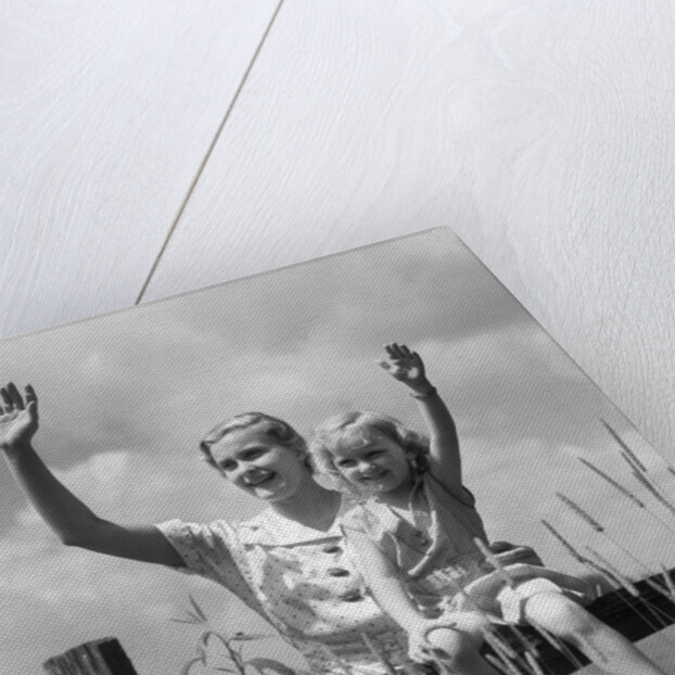 1930s girl sitting on fence with woman next to her in field waving by Anonymous