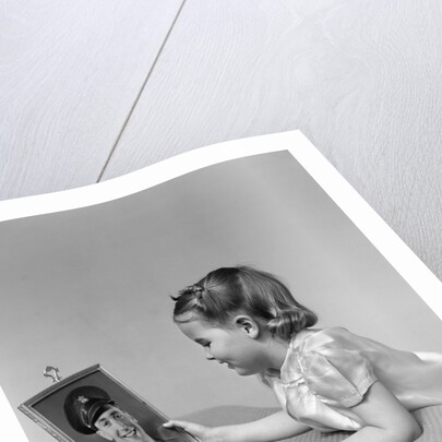 1940s child little girl looking at framed picture of her father a soldier in uniform by Anonymous