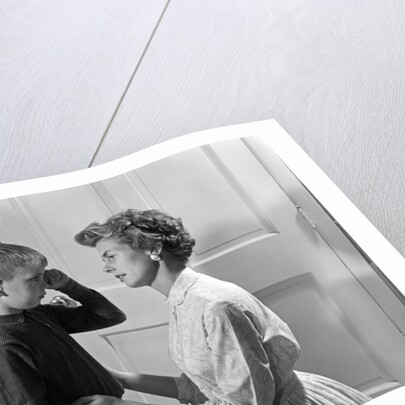 1960s sad crying boy rubbing his eyes is comforted or disciplined by his caring mother by Anonymous