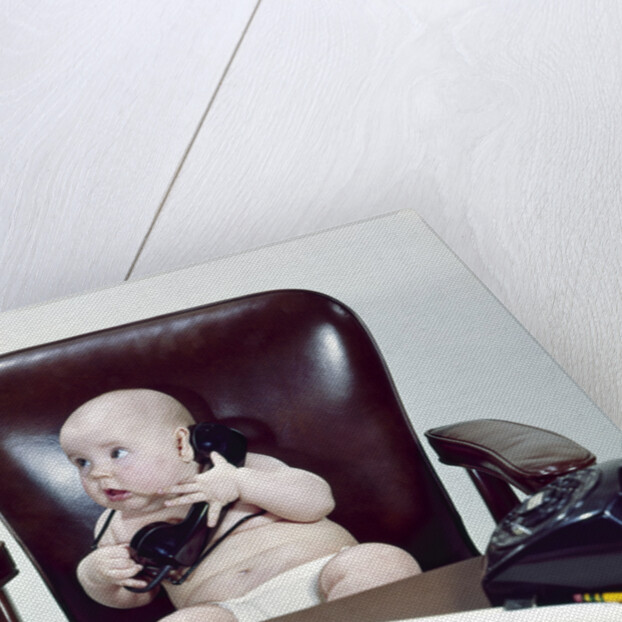 1960s chubby baby sitting in leather chair at office desk holding telephone by Anonymous