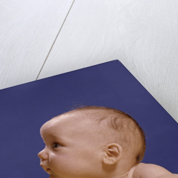1960s portrait of baby on yellow blanket resting on folded arms head turned to right looking up by Anonymous