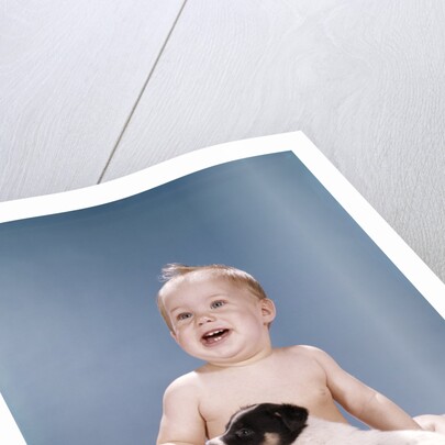 1960s smiling baby girl sitting in diapers playing with young black and white puppy dog by Anonymous