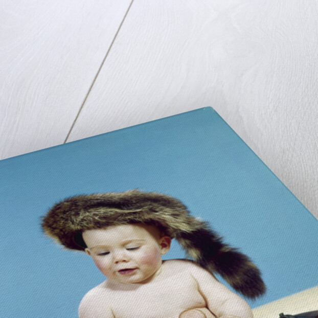 1960s baby boy wearing coonskin cap with stuffed animal and shotgun by Anonymous
