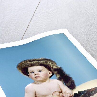 1960s baby boy wearing coonskin cap with stuffed animal and shotgun gun by Anonymous