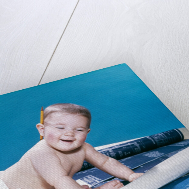 1960s baby eyes closed funny facial expression crawling on rolling out blueprints by Anonymous