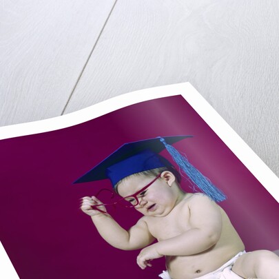 1960s graduate baby wearing mortarboard eyeglasses reading book by Anonymous