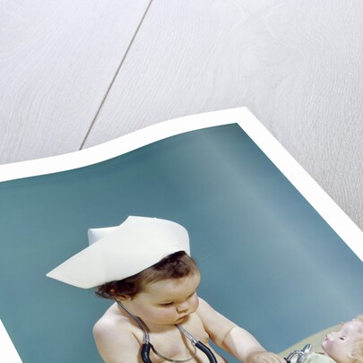 1960s baby wearing nurse nurse's cap stethoscope listening to doll heartbeat chest by Anonymous