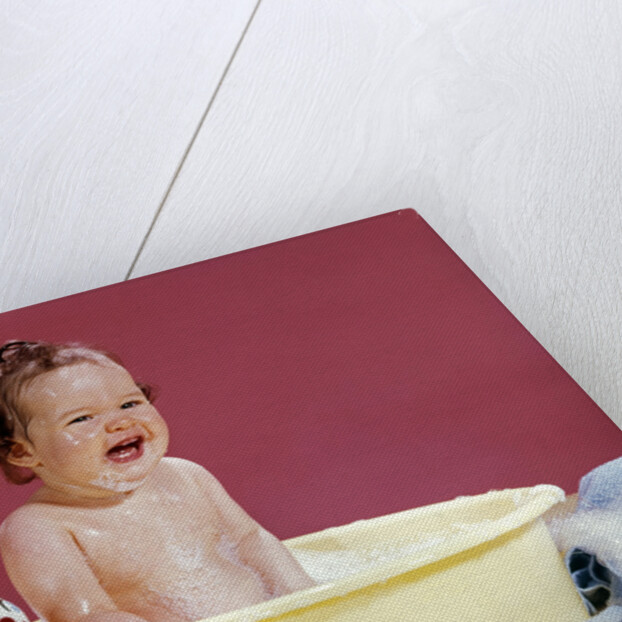 1960s crying brunette baby sitting in yellow plastic bath tub with toy clown by Anonymous