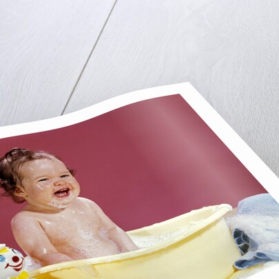 1960s crying brunette baby sitting in yellow plastic bath tub with toy clown by Anonymous