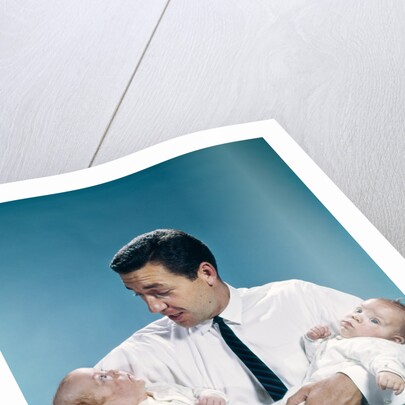 1960s father holding twin babies infants looking down at one of them by Anonymous