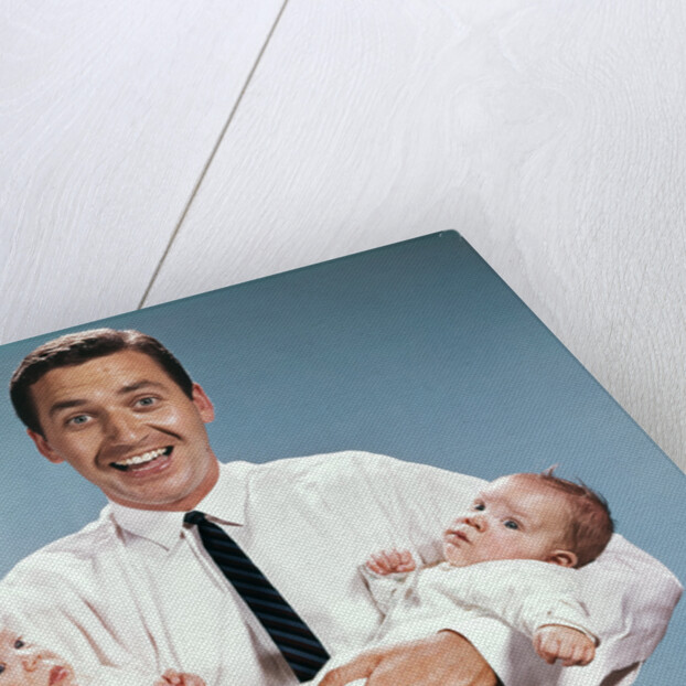 1960s smiling man father looking at camera holding twin babies infants by Anonymous