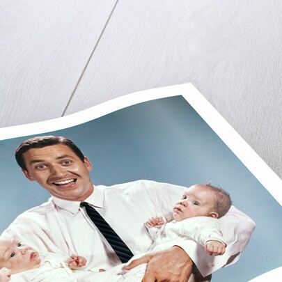 1960s smiling man father looking at camera holding twin babies infants by Anonymous