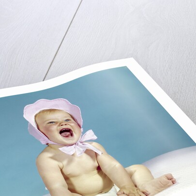 1960s baby wearing pink checked bonnet laughing by Anonymous