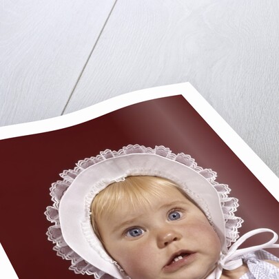 1960s portrait baby girl wearing bonnet and blue gingham dress showing two front teeth looking at camera by Anonymous