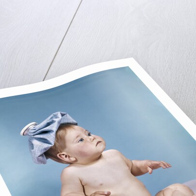 1960s baby sitting with ice pack on top of head by Anonymous