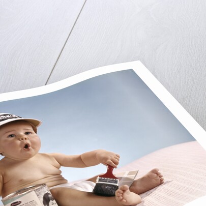 1960s baby with funny facial expression wearing painters cap holding paintbrush sitting by paint can by Anonymous