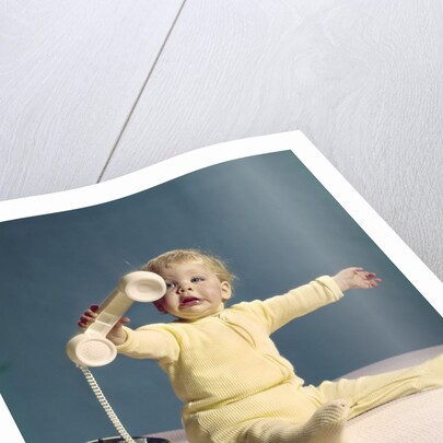 1960s baby holding telephone head set by Anonymous