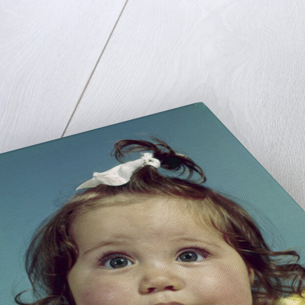 1960s brunette baby girl round chubby face yellow dress ribbon topknot interested sincere facial expression looking at camera by Anonymous